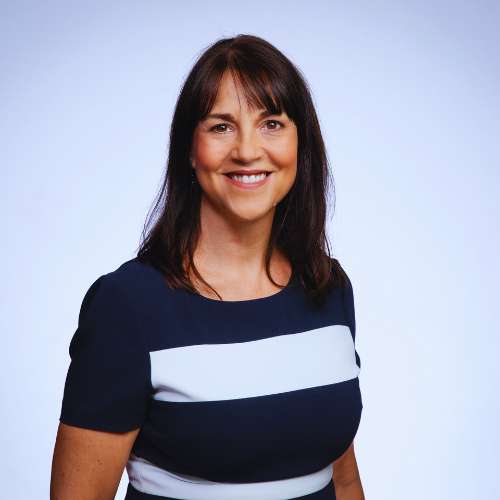 Professional headshot of a smiling woman with dark hair, wearing a navy top with a white stripe, set against a light neutral background.
